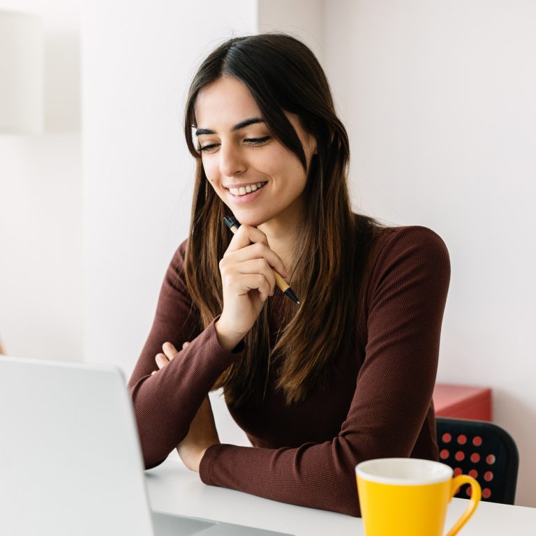Portrait of young adult student sitting on table using laptop learning online