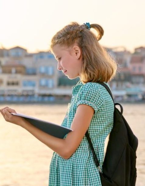 Girl child young student with backpack reading school notebook, outdoor